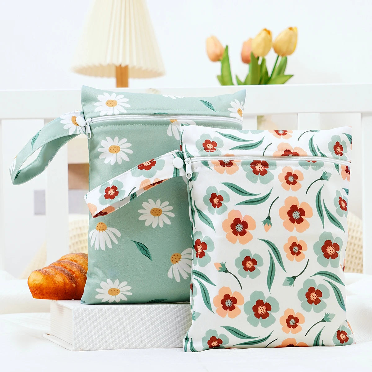A pair of light green fabric wet dry bags with white and orange floral patterns are displayed on a white surface.
