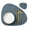 A set of dark gray reversible non-slip placemats with a white plate and silverware on a table.