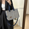 A woman holds a striped canvas tote bag with navy straps and inner pockets against a black coat.