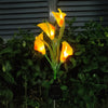 A bright yellow calla lily flower illuminated by a solar-powered LED light in a garden setting.