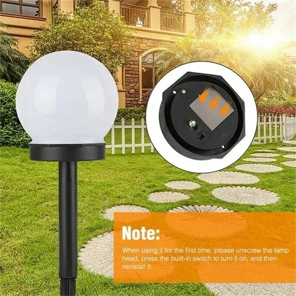 A black solar-powered LED garden bulb with a spherical white light head installed in a grassy outdoor setting.
