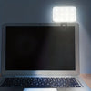 A laptop is illuminated by a clip-on LED light, highlighting the screen and keyboard.