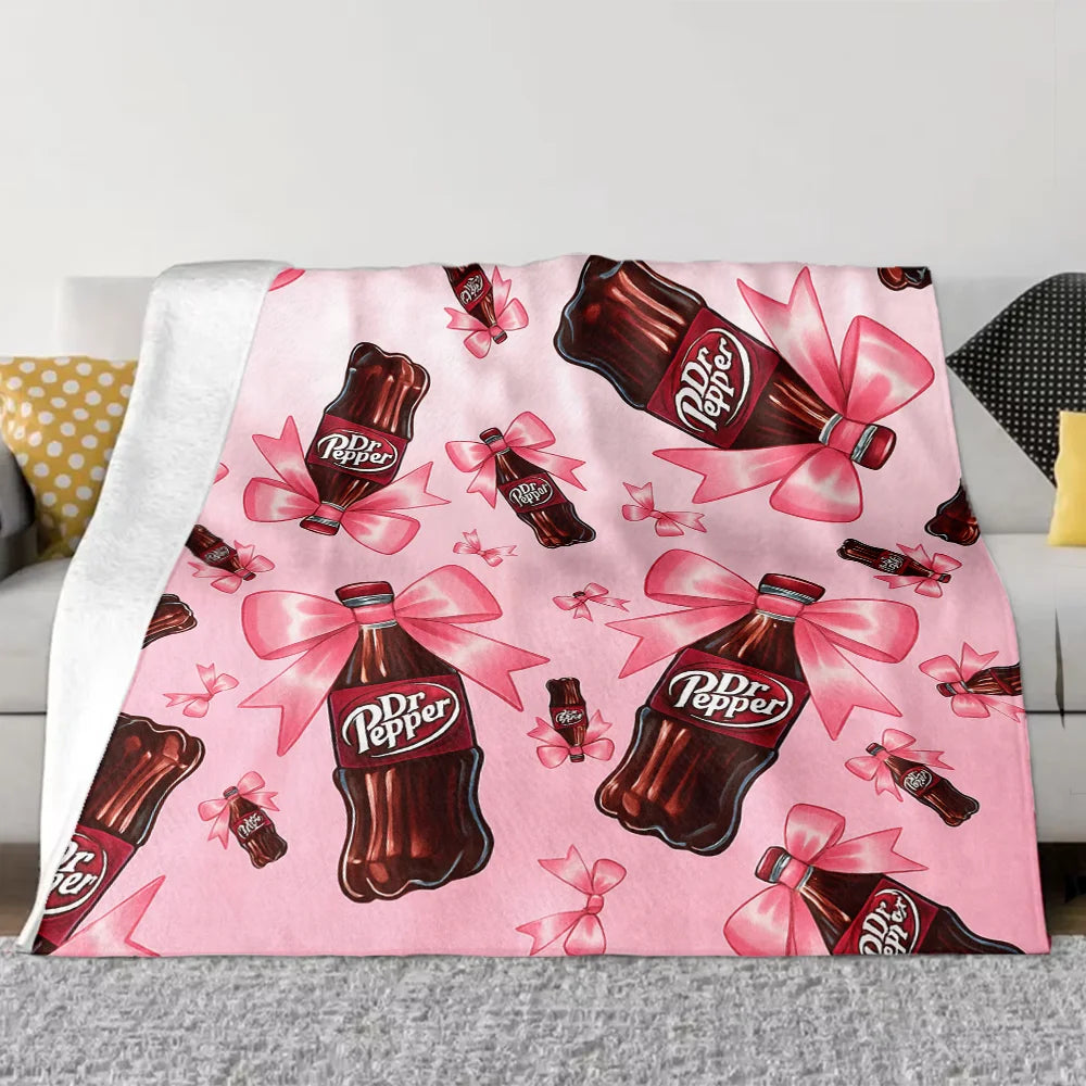 A pink throw blanket featuring a repeating pattern of Dr. Pepper bottles with pink ribbons.