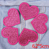 A set of five pink glitter heart iron-on patches placed on a denim fabric background.