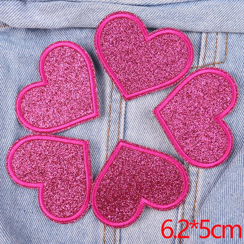 A set of five pink glitter heart iron-on patches placed on a denim fabric background.