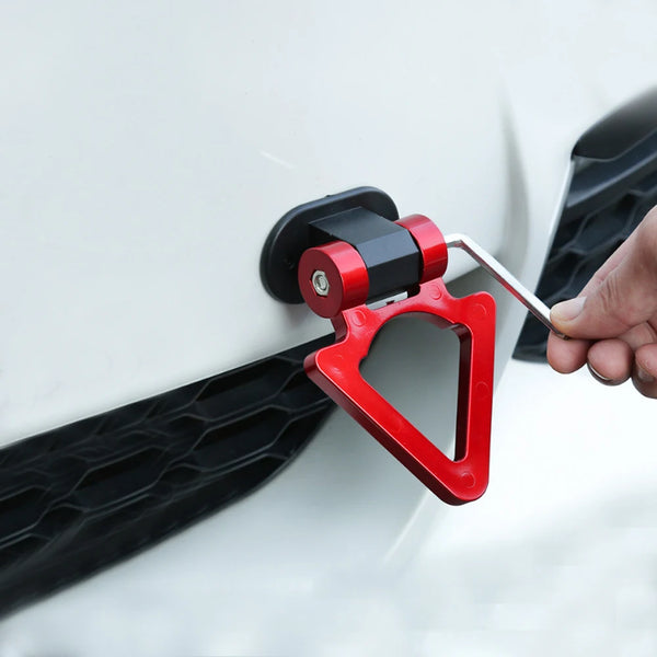 A hand is attaching a red racing style tow hook decoration to the side of a white car.