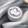 A roll of soft, colorful gradient cake yarn is displayed on a gray fabric background.