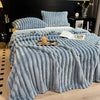 A light blue fluffy flannel blanket draped over a bed, featuring vertical pleats and topped with a wooden tray.