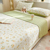 A floral quilted bedspread in white and yellow patterns with a green dust-proof cover and matching pillows.