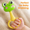 A hand is holding a green, frog-shaped sensory rattle toy designed for baby grabbing practice.