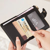A hand holds a black compact zippered wallet with card slots and a transparent window displaying an ID.