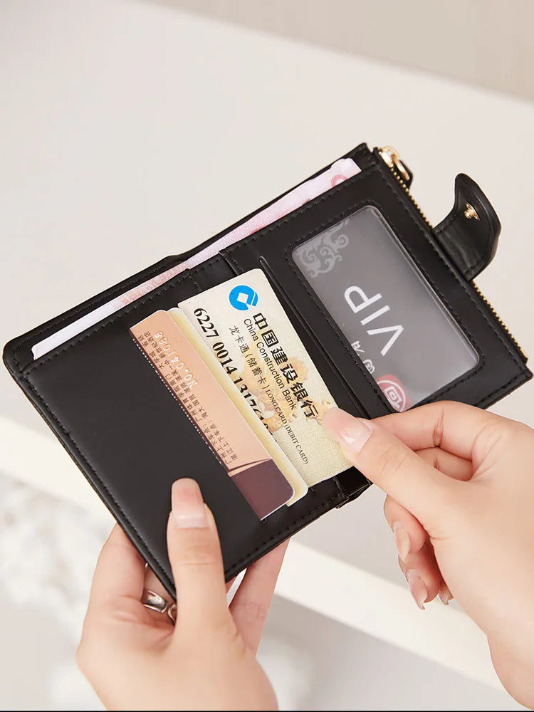 A hand holds a black compact zippered wallet with card slots and a transparent window displaying an ID.