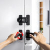 A hand is shown rotating a black non-drill child safety door lock on a white appliance cabinet door.