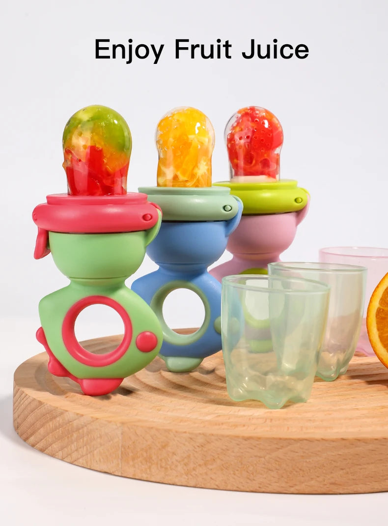 A set of colorful rotating silicone baby fruit feeders with dinosaur designs displayed on a wooden board.