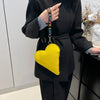 A yellow heart-shaped coin purse with a black strap is held by a person wearing a black blazer.