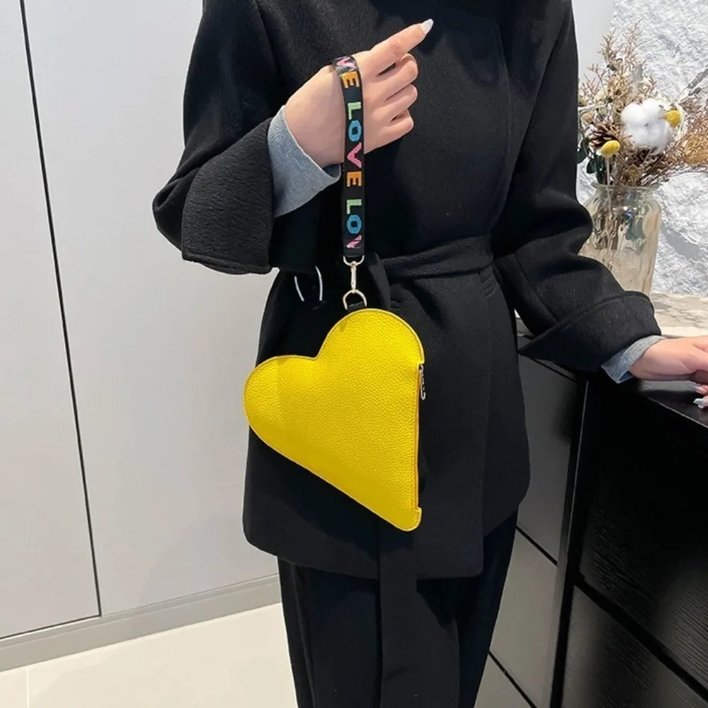 A yellow heart-shaped coin purse with a black strap is held by a person wearing a black blazer.