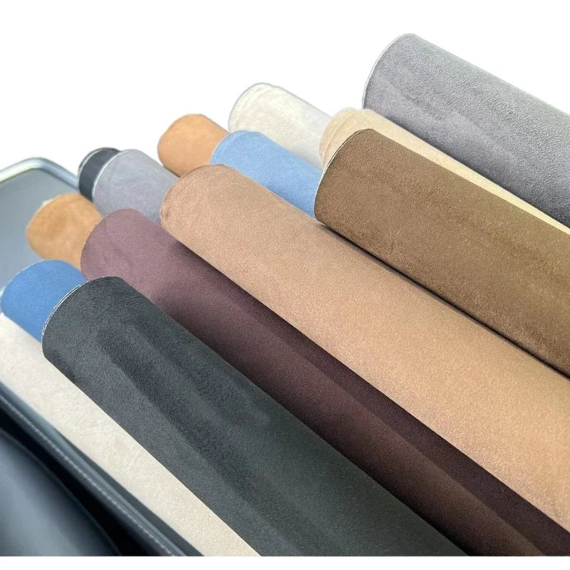 A collection of self-adhesive suede fabric rolls in various earth tones and neutrals, displayed in a row.