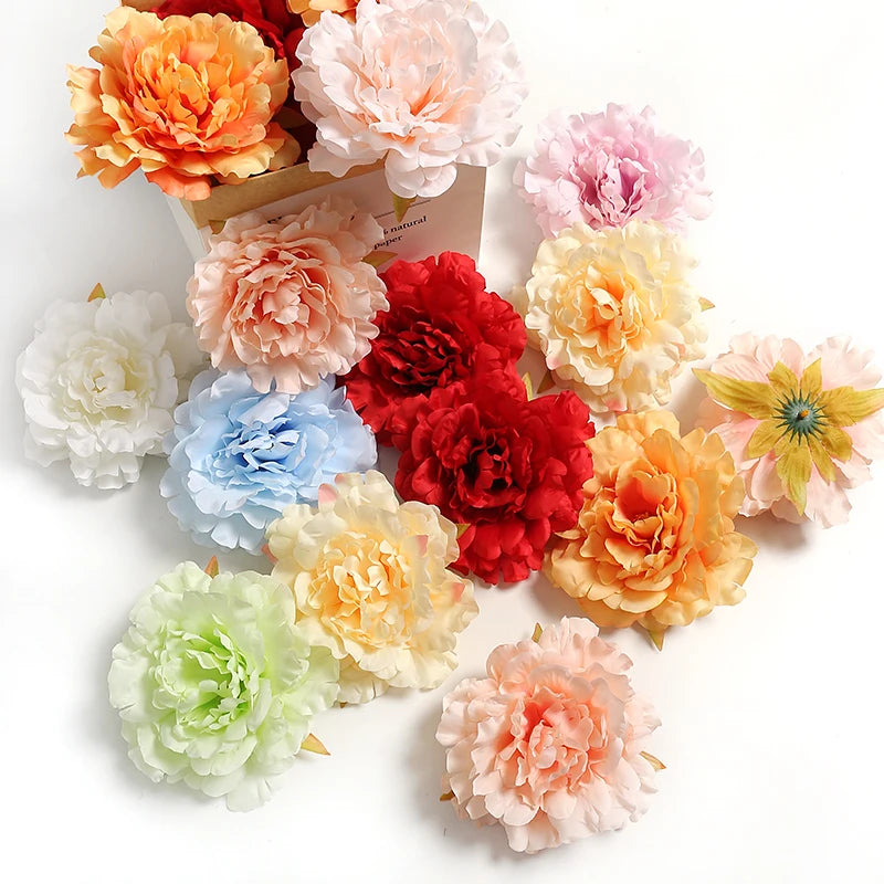 A collection of lifelike silk peony flower heads in various shades of peach, pink, orange, and yellow.