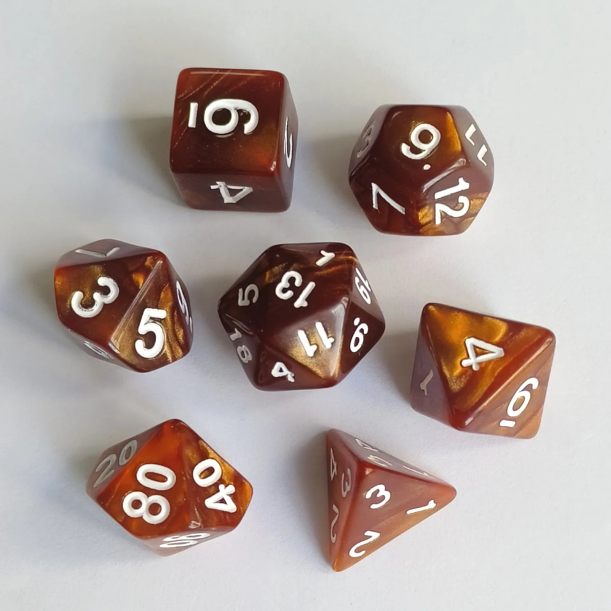 A collection of seven polyhedral dice in various colors and angles scattered on a white surface.