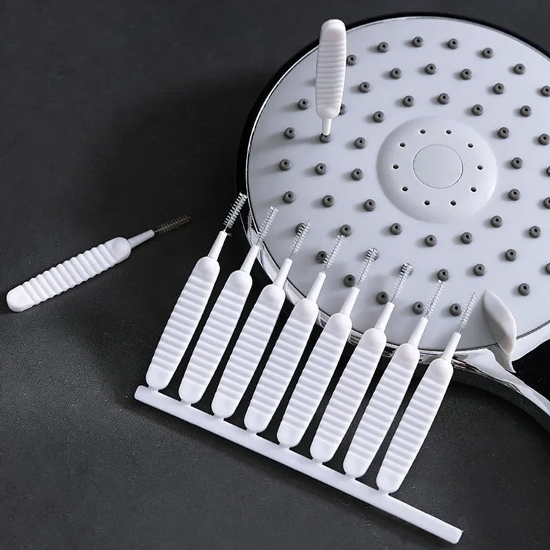 A white shower cleaning brush set with multiple nozzles and a handle is shown on a dark surface.