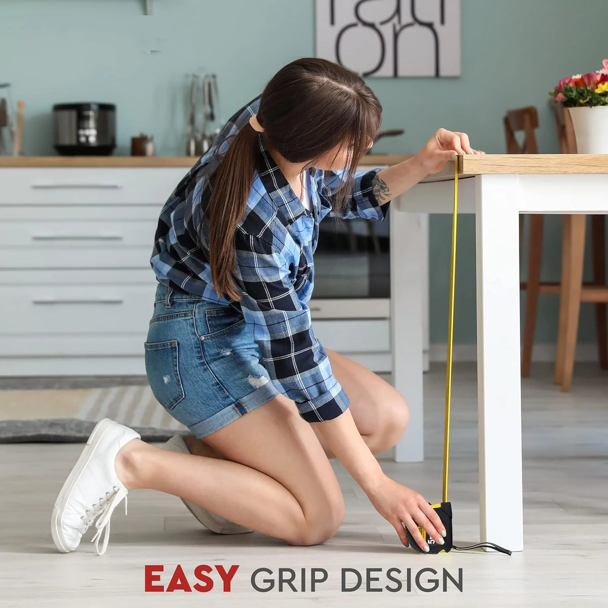 A person is using a yellow heavy-duty retractable measuring tape on a white table surface.