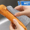 Eine Hand benutzt ein wiederverwendbares, nicht zerkratzendes Stahlwolle-Tuch, um eine orange Karotte in einer Küchenspüle zu