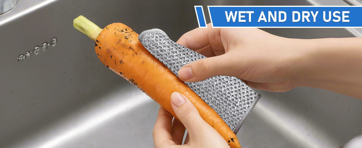 Eine Hand benutzt ein wiederverwendbares, nicht zerkratzendes Stahlwolle-Tuch, um eine orange Karotte in einer Küchenspüle zu