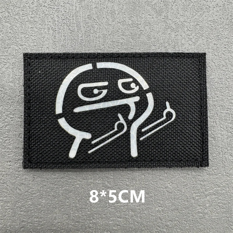 Black embroidered patch featuring a stylized, grinning face design on a gray background.