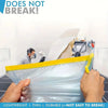 A hand is wrapping a clear plastic film around a surface, demonstrating the durability of pre-taped masking film.