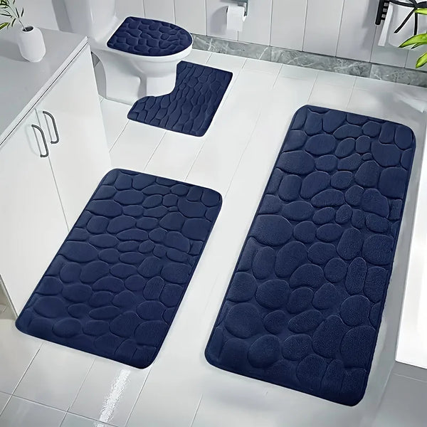A set of dark blue pebble-embossed quick-dry bath mats placed on a white tiled floor next to a toilet.