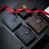 A collection of black and brown genuine leather wallets and a red ribbon on a dark surface.