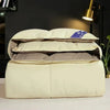 A stack of a luxury white goose and duck down comforter with a cotton cover resting on a white surface.
