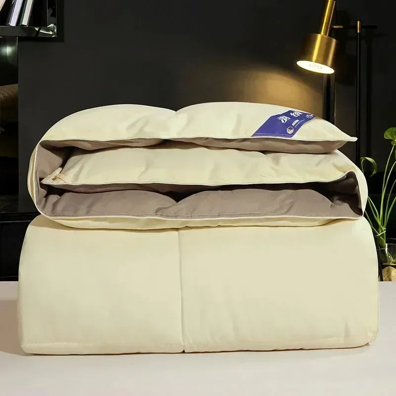 A stack of a luxury white goose and duck down comforter with a cotton cover resting on a white surface.