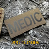 A dark olive green medical patch with the word MEDIC embroidered on it, placed on a rough gray stone surface.