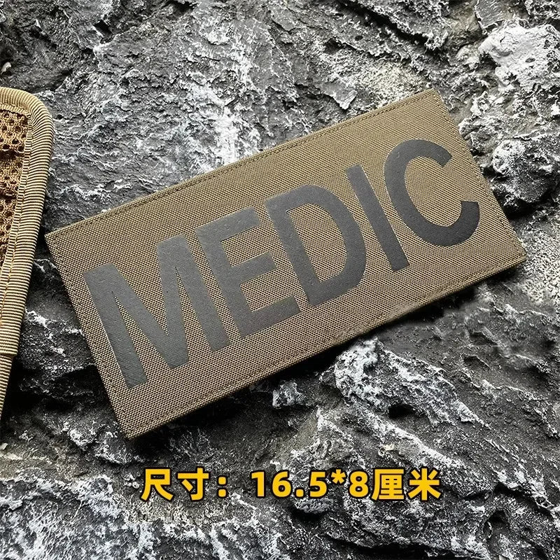 A dark olive green medical patch with the word MEDIC embroidered on it, placed on a rough gray stone surface.