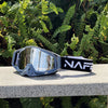 A pair of gray HD Motocross goggles with a reflective lens and a black strap resting on a light surface.