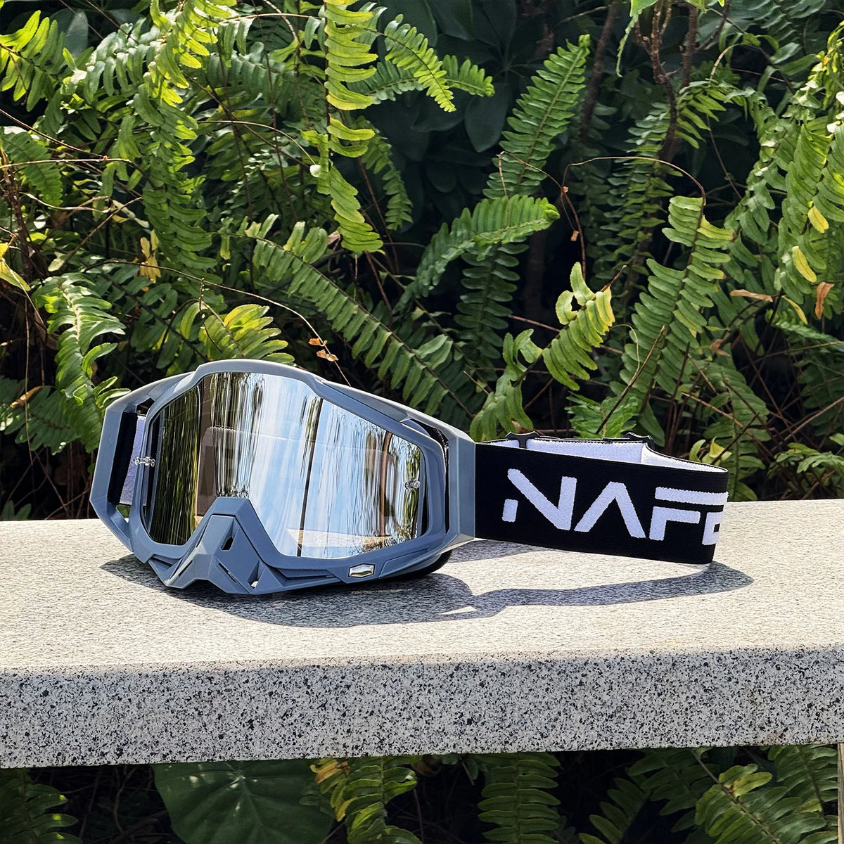 A pair of gray HD Motocross goggles with a reflective lens and a black strap resting on a light surface.