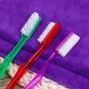 A set of six premium hard bristle toothbrushes in various colors, including green, red, and purple, resting on a purple towel
