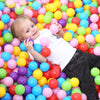 A toddler is smiling while surrounded by a large pile of colorful plastic ball pit balls.