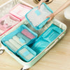 A light green packing cube set with six individual cubes and a mesh pouch is shown in an open storage box.