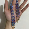 A hand holds a long, iridescent blue and purple resin chain replacement strap for handbags.