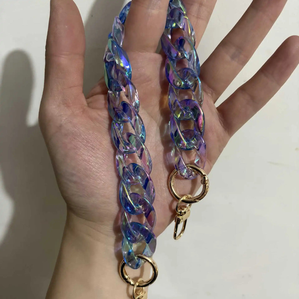 A hand holds a long, iridescent blue and purple resin chain replacement strap for handbags.