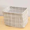 A light beige cotton and linen storage basket with a grid pattern is shown on a wooden surface.