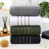 A stack of three gold-striped towels in various shades of gray, green, and navy blue on a white surface.