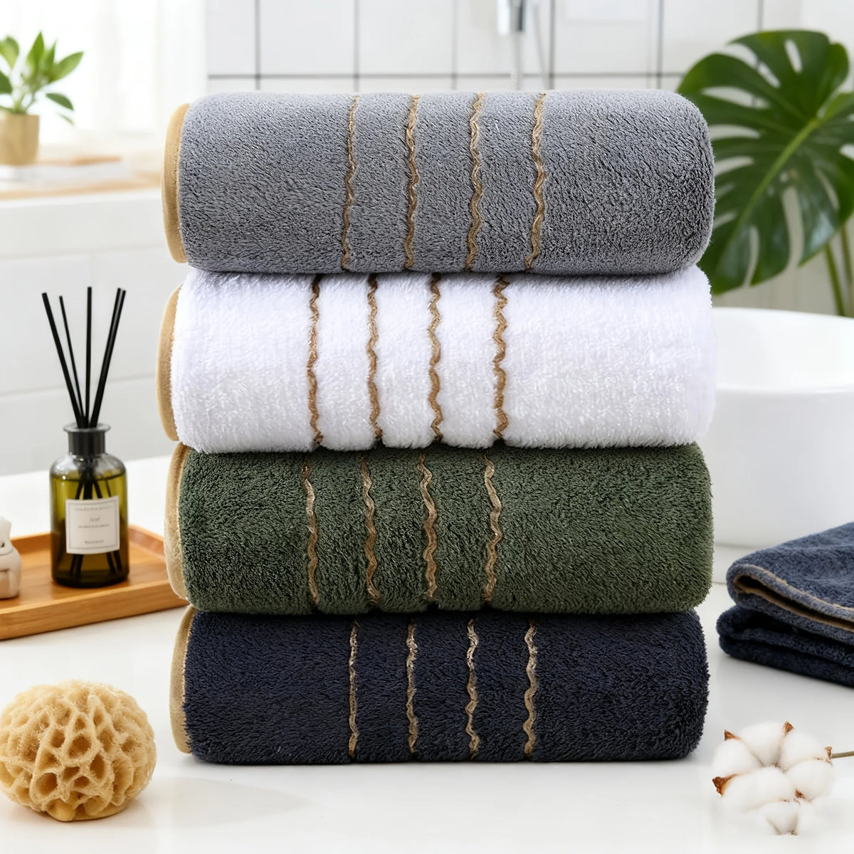 A stack of three gold-striped towels in various shades of gray, green, and navy blue on a white surface.