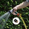 A hand is using a garden hose quick connector set to spray water onto green foliage.