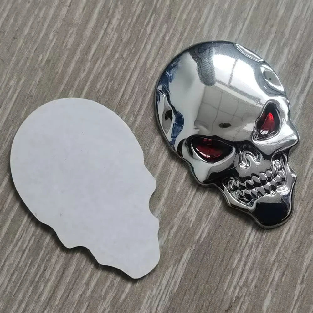 A chrome skull emblem badge featuring a red eye, placed next to its white backing.