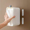 A hand is holding a white picture hanging strip dispenser against a beige wall.
