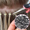 A hand holds a pink tool with a needle to install hair extensions using silicone-lined micro rings.
