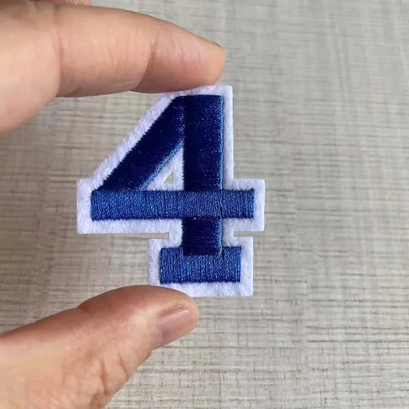 A hand holds a dark blue iron-on 3D number patch shaped like the numeral four.